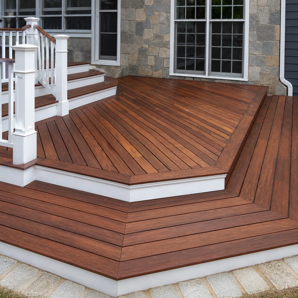 Refinished mahogany deck with a mitred border and white fascia, meeting a stone and shingle house, by Genesis Pro Painting in Westchester NY