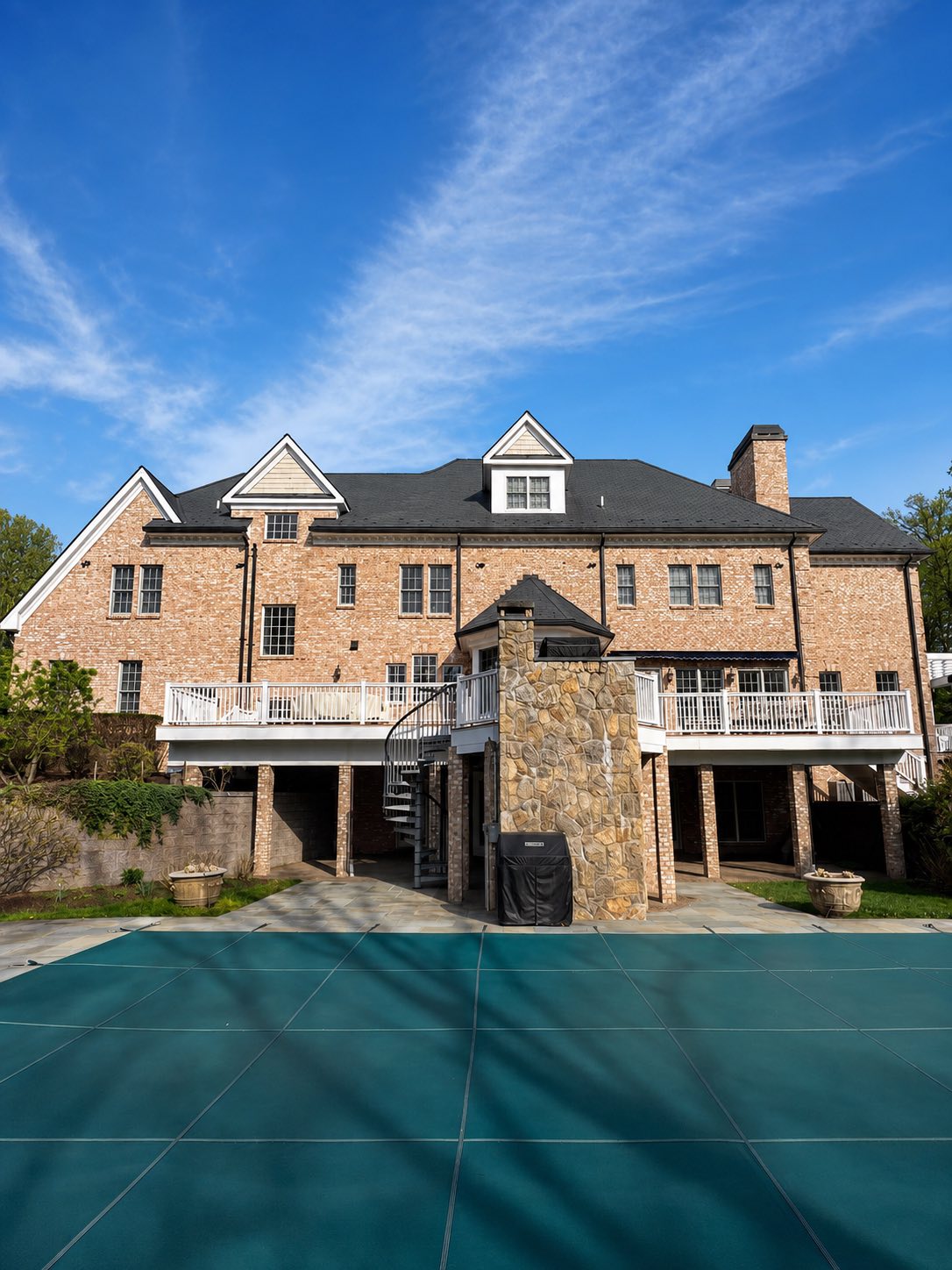 Rear exterior of a brick home with freshly painted white deck railings and poolside trim by Genesis Pro Painting