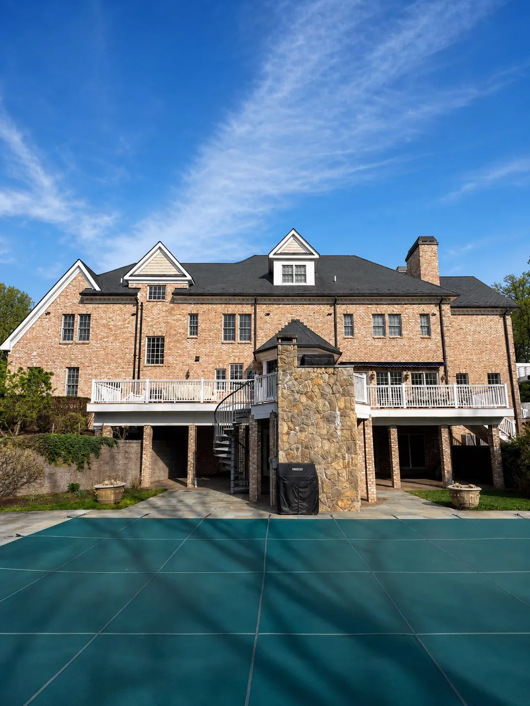 Rear exterior of a brick home with freshly painted white deck railings and poolside trim by Genesis Pro Painting