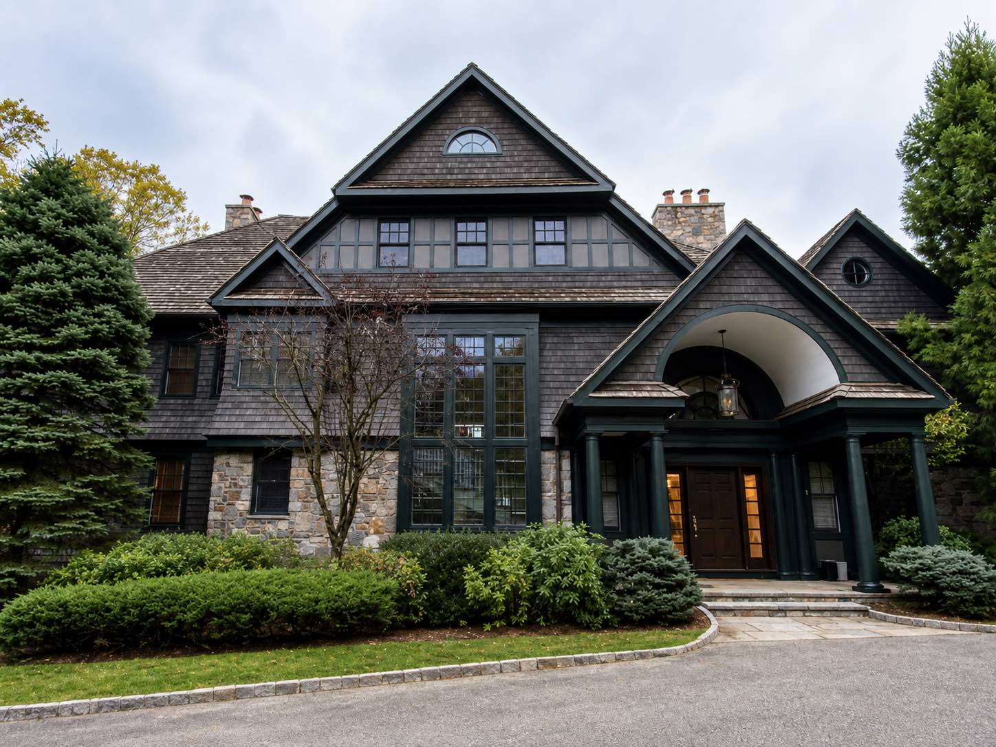 Exterior painted shingle-style home with dark green trim, columns, and stone base by Genesis Pro Painting in Westchester NY