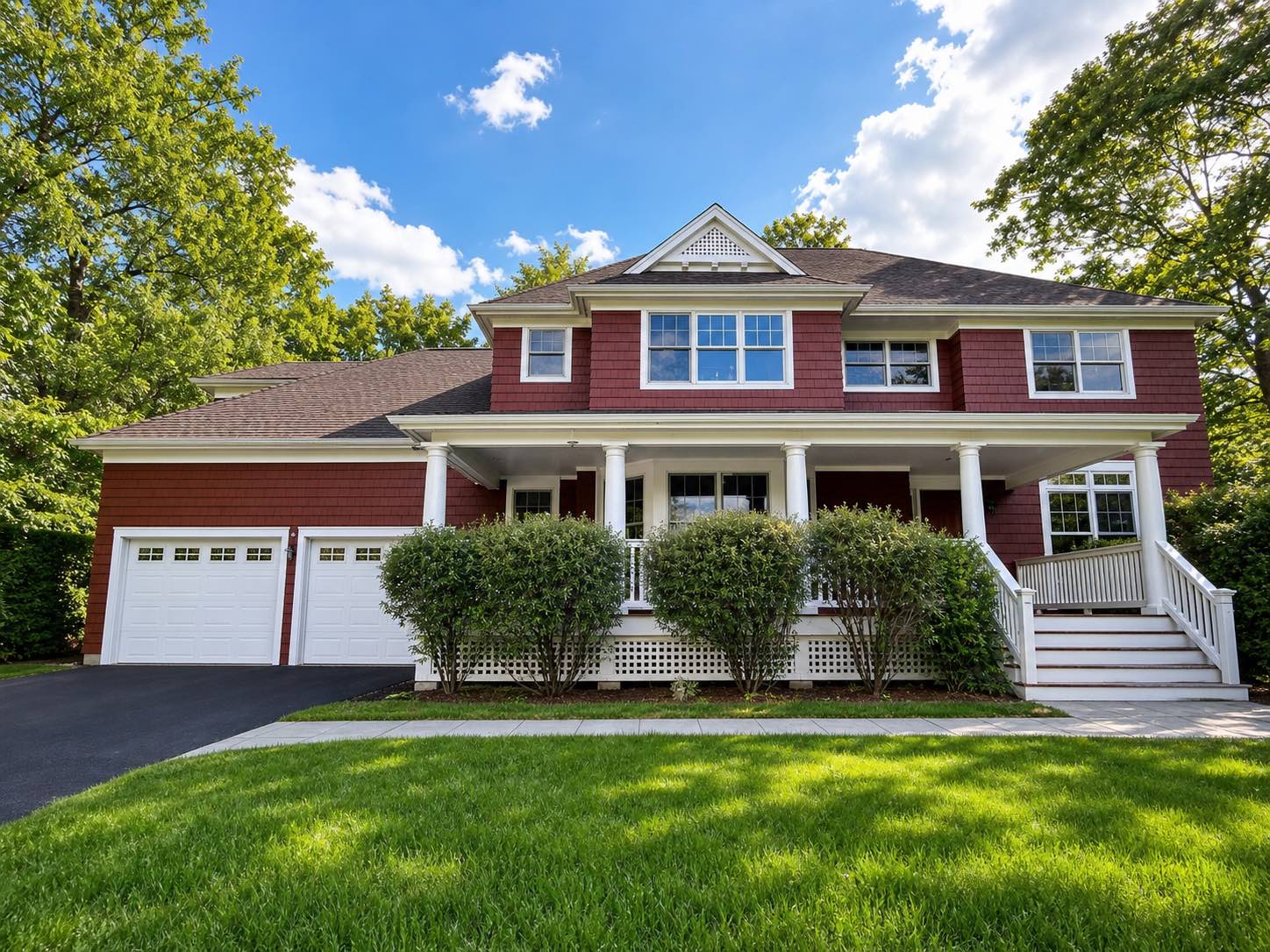 Exterior painted shingle home with deep red siding, white trim, columns, and porch railings by Genesis Pro Painting