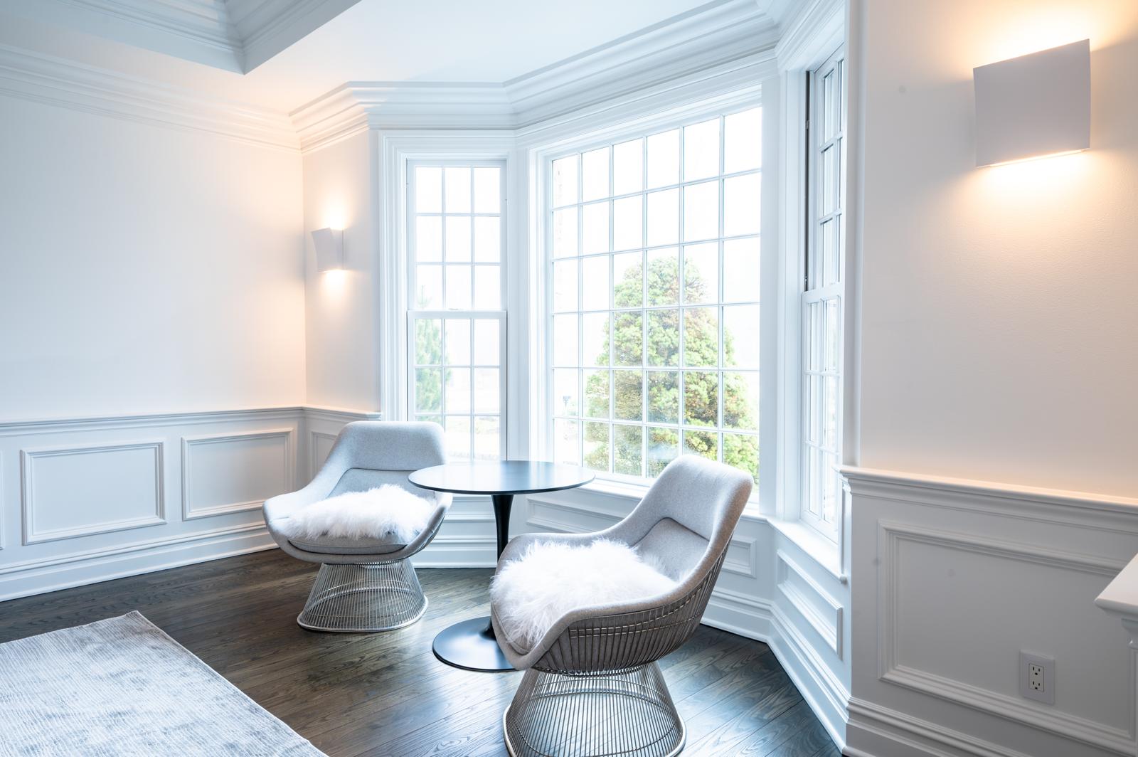 Bright white sitting nook with wainscoting, a bay window, and detailed trim painted by Genesis Pro Painting