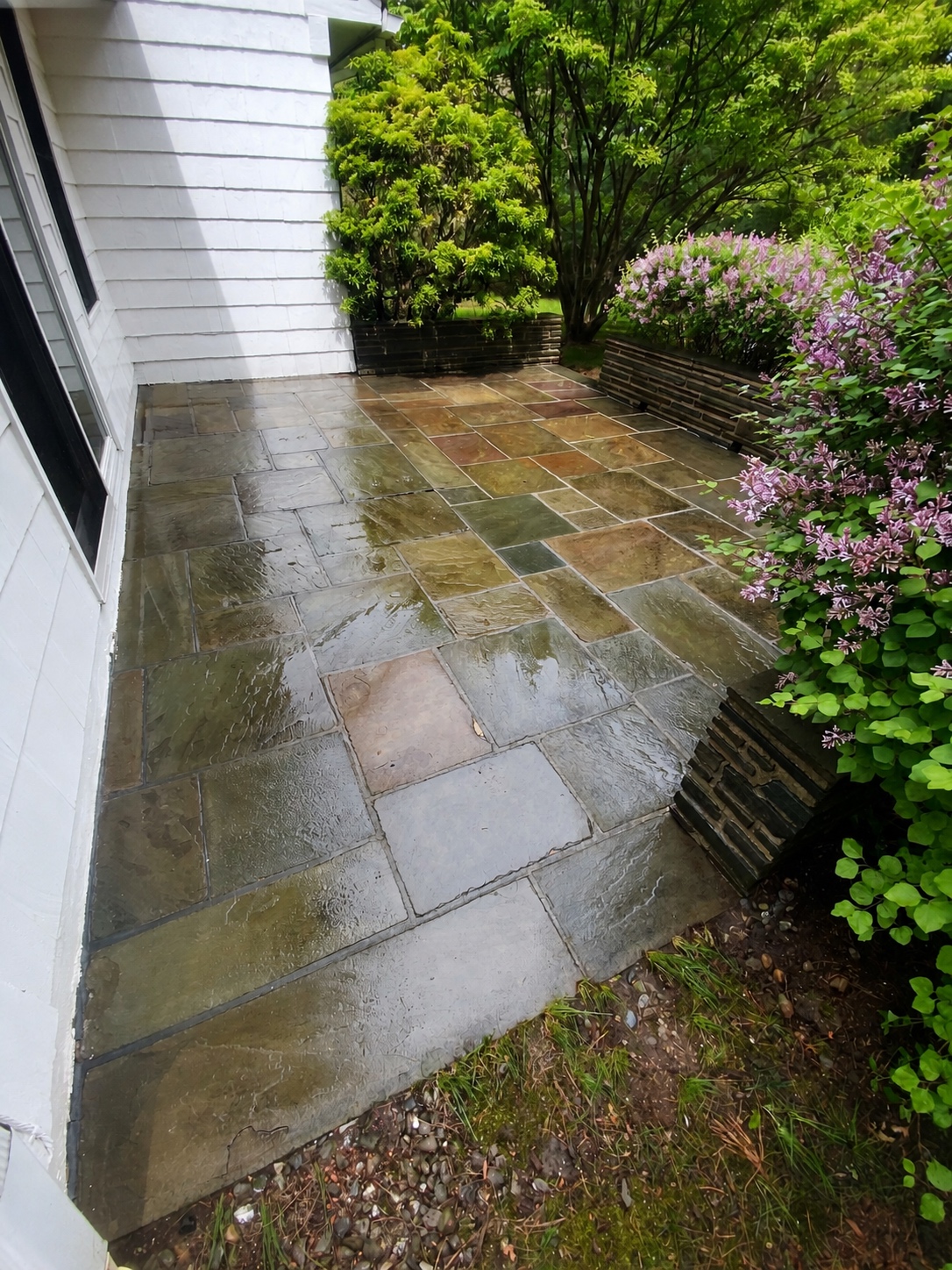 Clean stone patio beside a landscaped home after pressure washing by Genesis Pro Painting