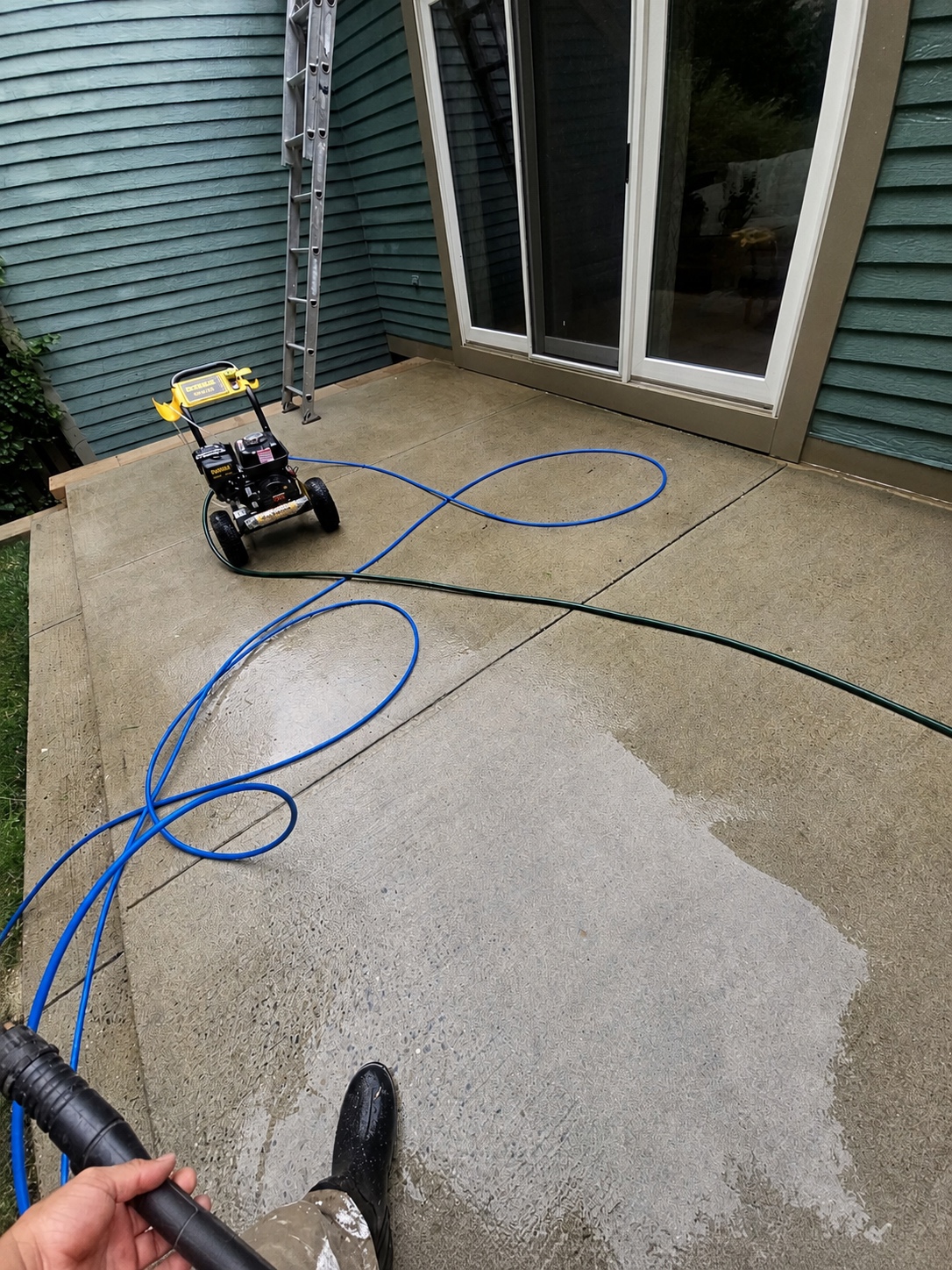 Concrete patio being pressure washed with equipment and hose visible by Genesis Pro Painting in Westchester NY