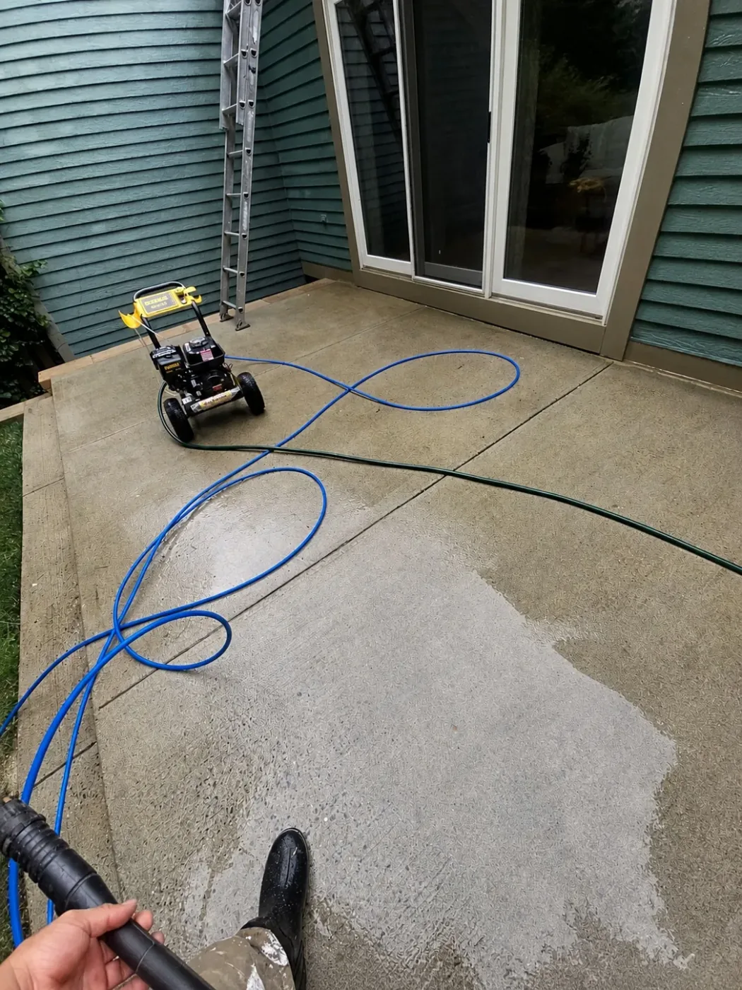 Concrete patio being pressure washed with equipment and hose visible by Genesis Pro Painting in Westchester NY
