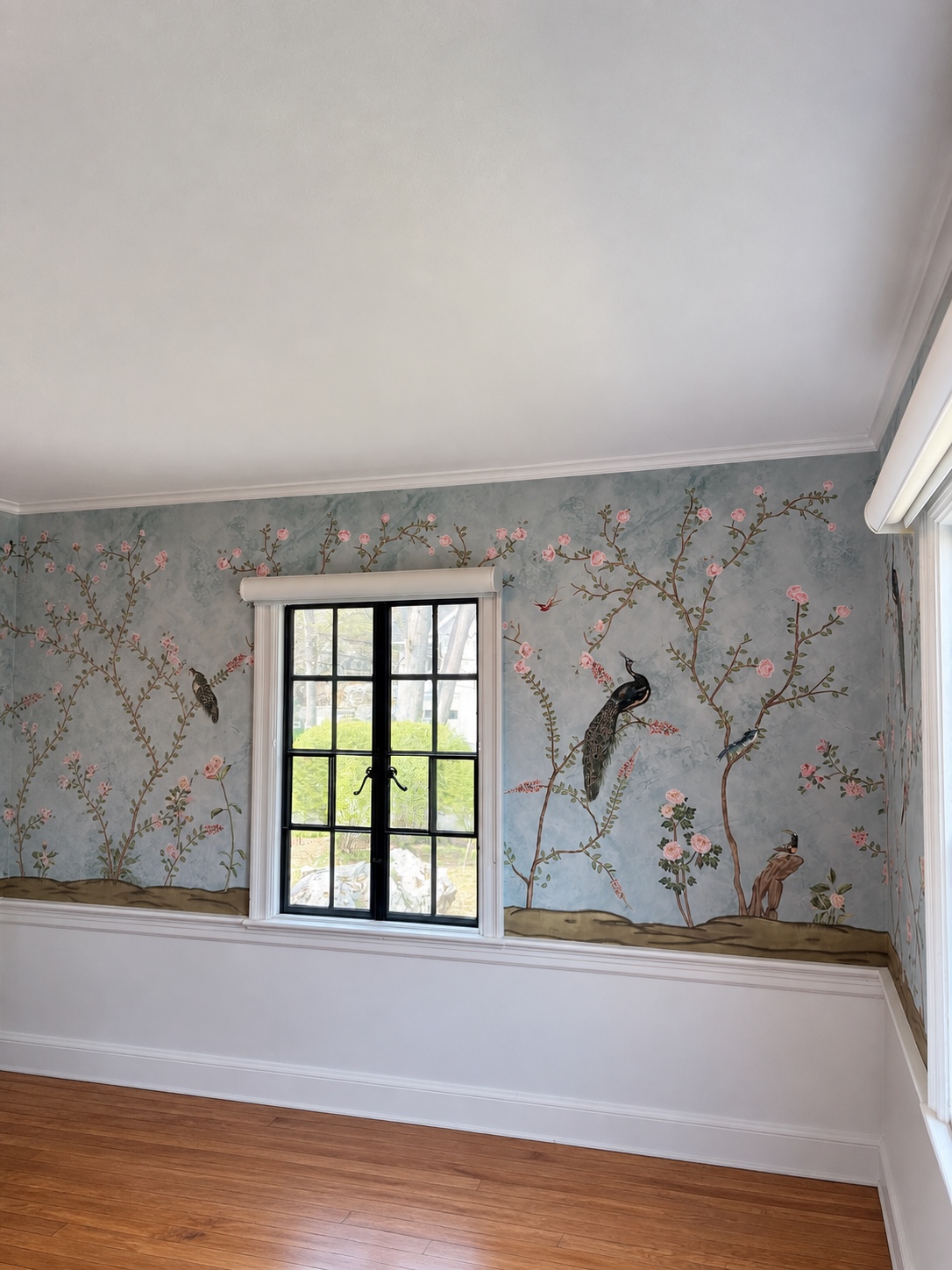 Blue-grey chinoiserie wallpaper with roses and a peacock, run around a window and finished into the crown molding and chair rail, by Genesis Pro Painting in Westchester NY