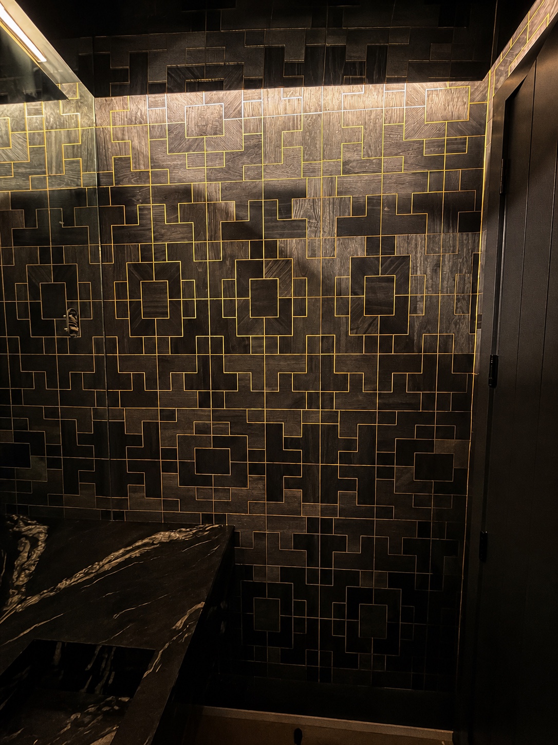 Dark geometric wallpaper with gold linework installed in a modern bathroom by Genesis Pro Painting