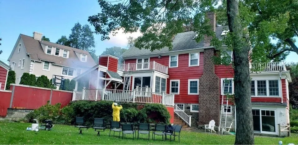 Worker washing red house siding before an exterior repaint