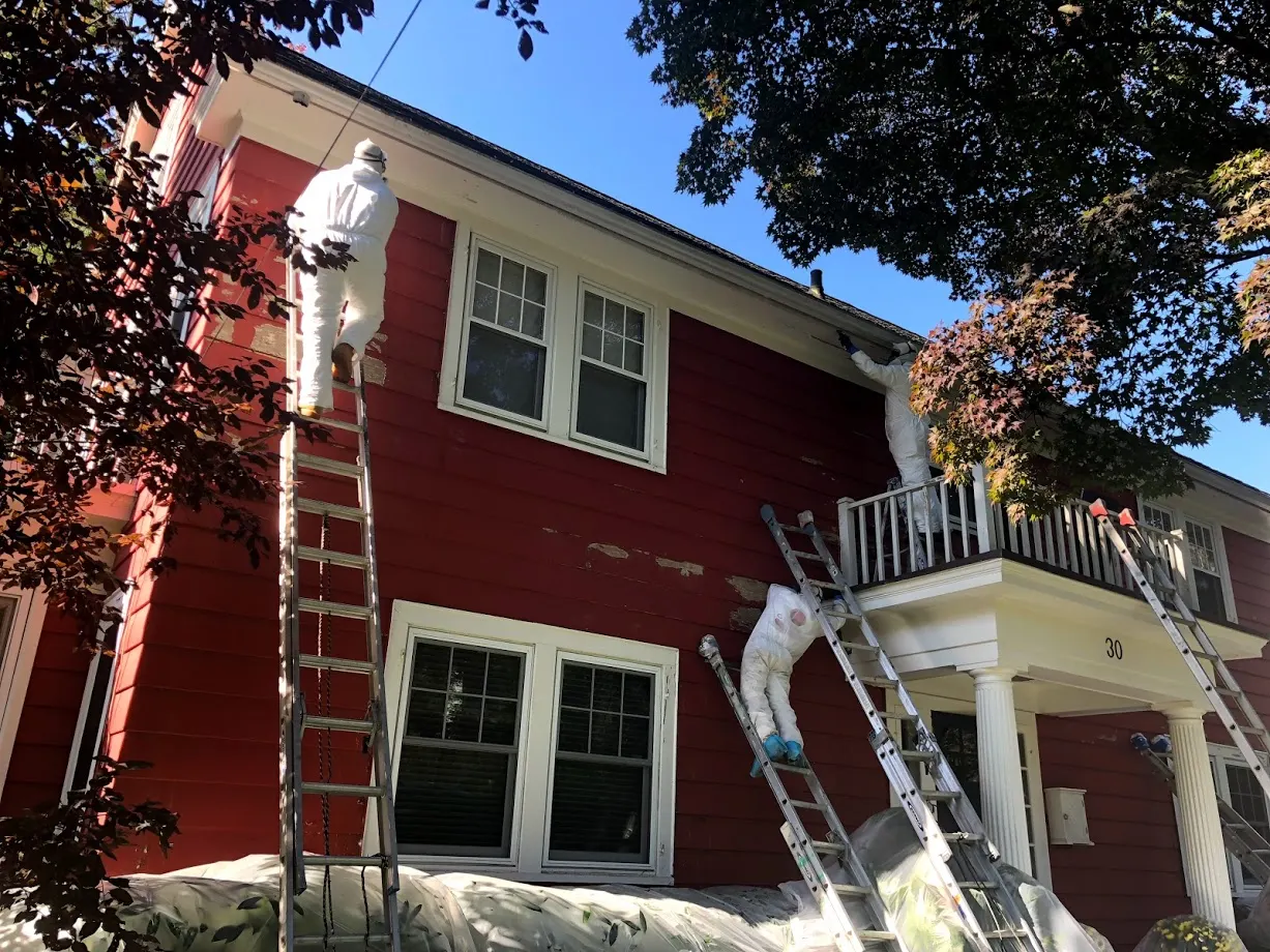Crew in protective coveralls preparing an older red-sided house