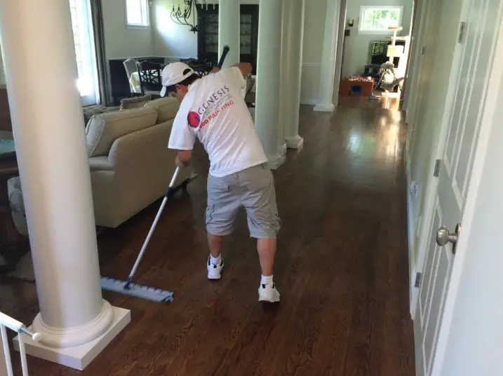 Genesis Pro Painting worker cleaning a wood hallway floor after painting
