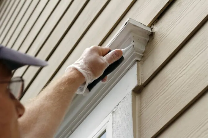 Worker caulking the joint above an exterior window before painting