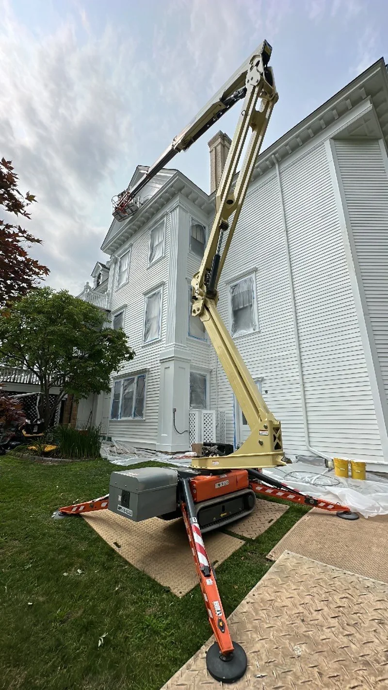 Boom lift beside a white building with protected windows and ground surfaces